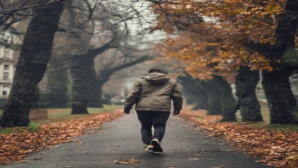 A person walking briskly along a tree lined urban path in British weather wearing everyday clothes